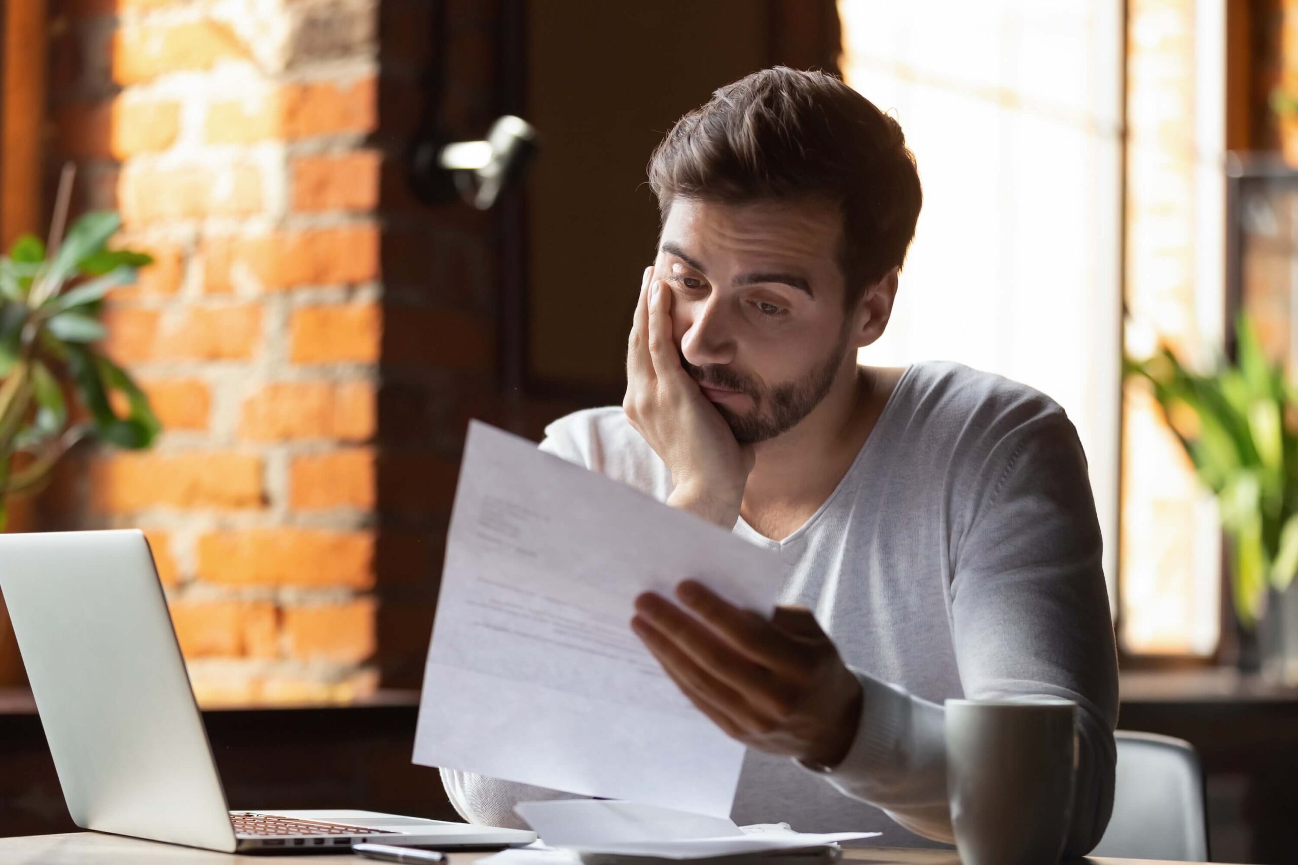 Frustrated confused young man reading a letter in a cafe, debt notification